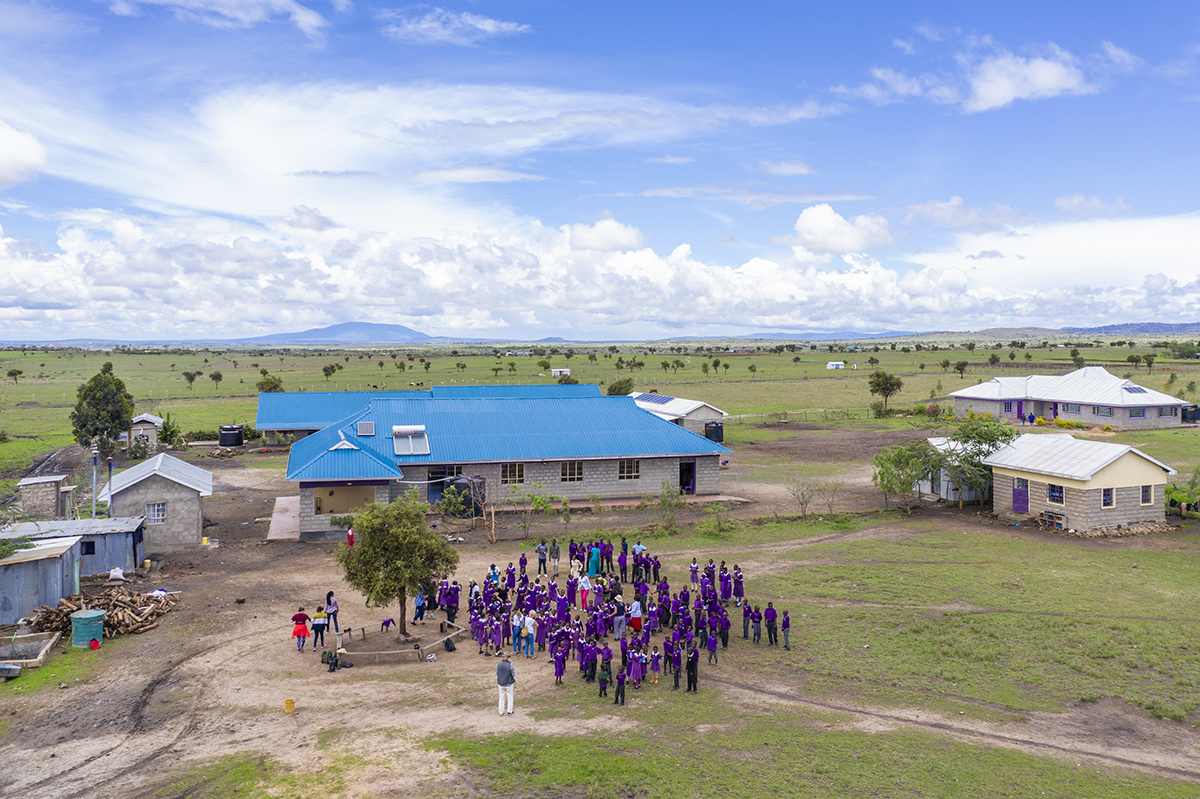 Skolbyggnad med blått tak med grupper av barn framför i i lila klädsel